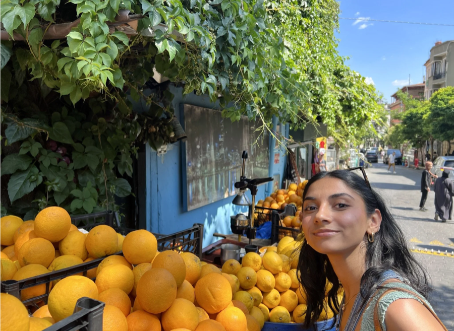 Pooja grinning next to a mountain of oranges at a juice stand